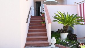 A staircase leading to a door, a potted plant, and a striped awning.