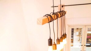 A modern living room with a black sofa, two orange cushions, a glass coffee table with a potted plant, and a unique ceiling light fixture. - Great Studio in amazing location (Jérusalem)