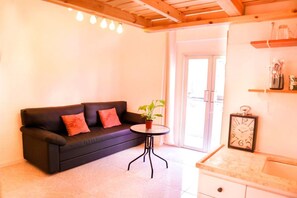 Un salon chaleureux avec un canapé noir, une petite table ronde agrémentée d’une plante et un plafond en bois.