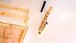 A room with a wooden staircase leading to a loft area, a flat-screen TV on a wooden shelf, and a string of warm light bulbs. - Great Studio in amazing location (Jérusalem)