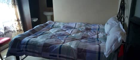 Un lit avec une couvre-lit à carreaux, un tapis rouge, un oreiller blanc et une tête de lit noire.
