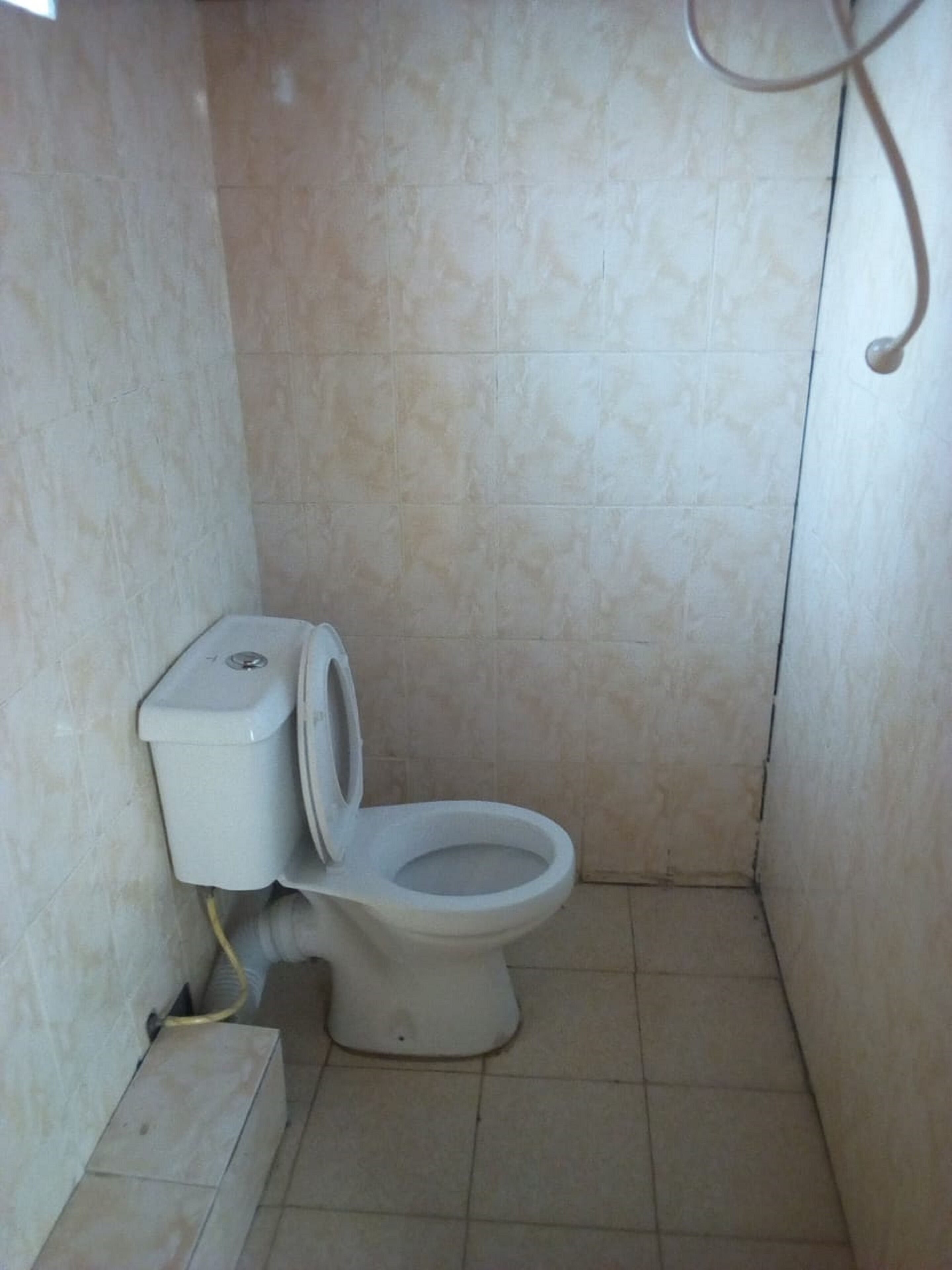 Un baño pequeño con azulejos, un inodoro, una tubería a la vista y un accesorio fijado a la pared.