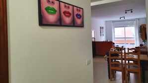 Un comedor con sillas de madera y una mesa, una cocina al fondo, y un cuadro en la pared con labios de varios colores.