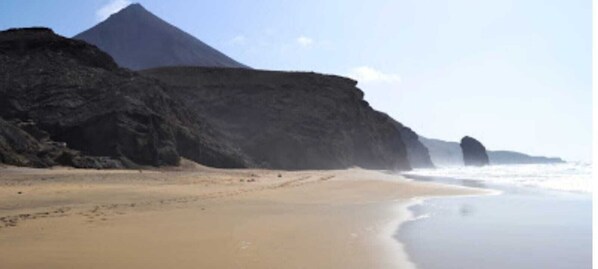 Une plage avec une grande formation rocheuse en arrière-plan et un ciel dégagé.