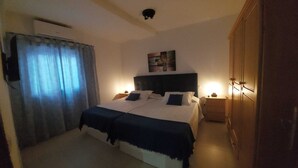 Un dormitorio con cama, cabecera, mesita de noche, armario y lámpara en el techo.