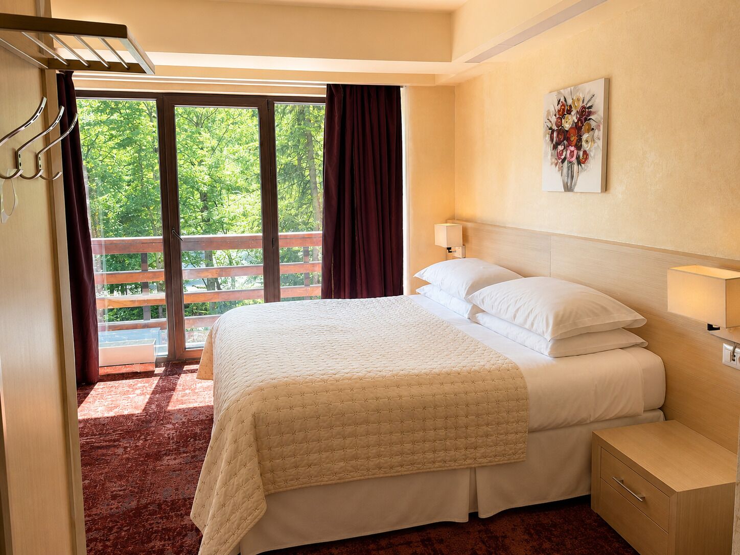 A hotel room with a bed, a nightstand, a lamp, a painting, and a balcony with curtains.