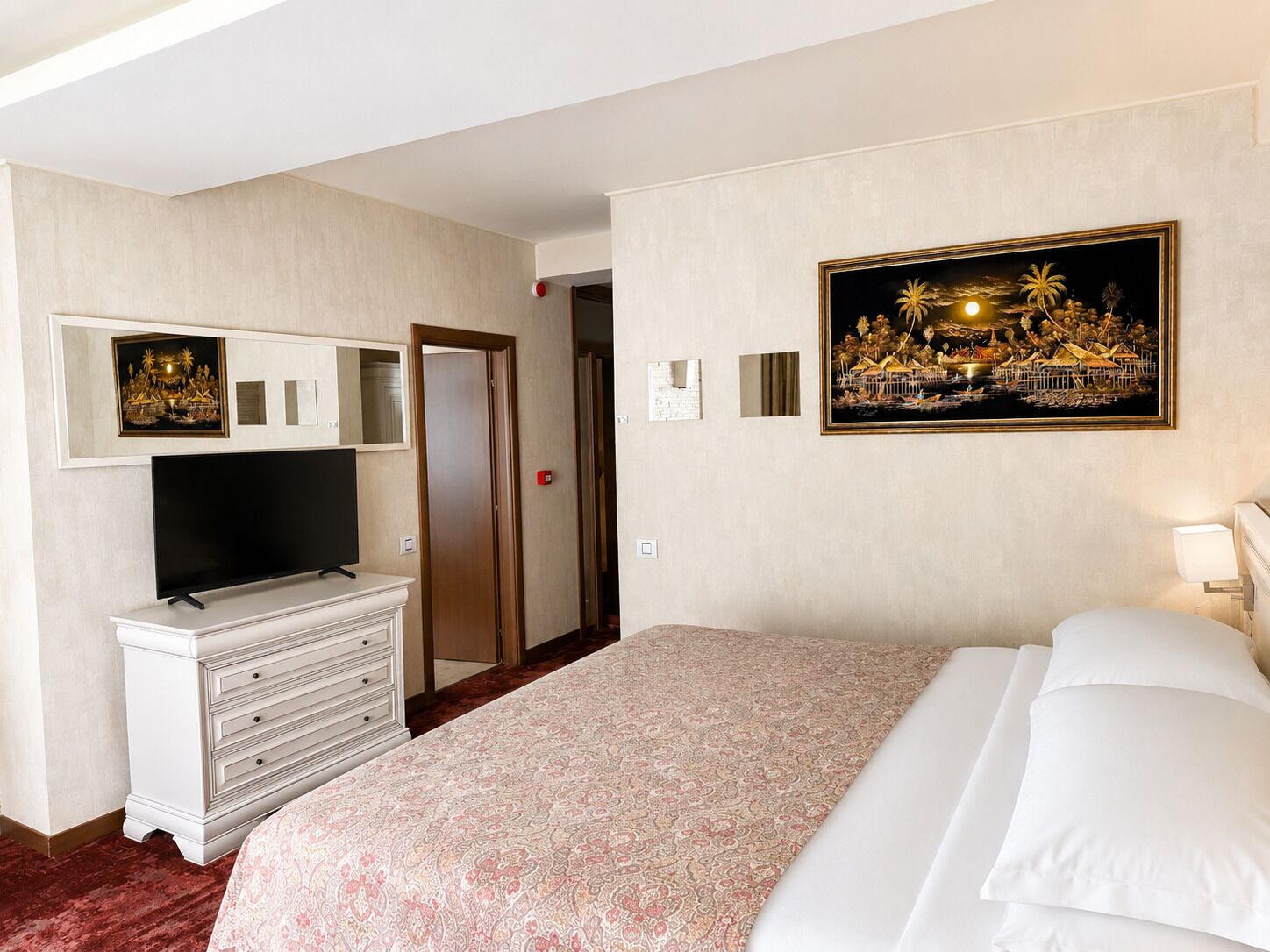 A hotel room with a bed, a dresser, a television, a painting, and a door.