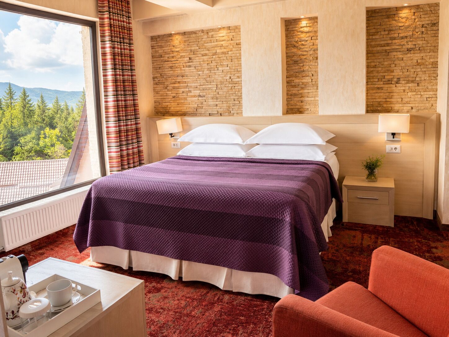 A hotel room with a bed, nightstands, a window with curtains, a view of trees, and a red carpet.