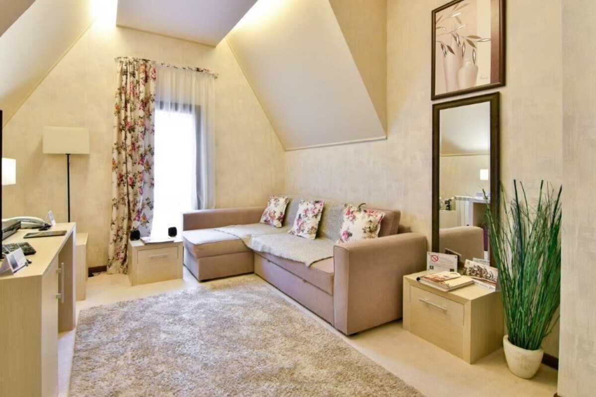 A cozy room with a sofa, a desk, a lamp, a large mirror, and a potted plant.