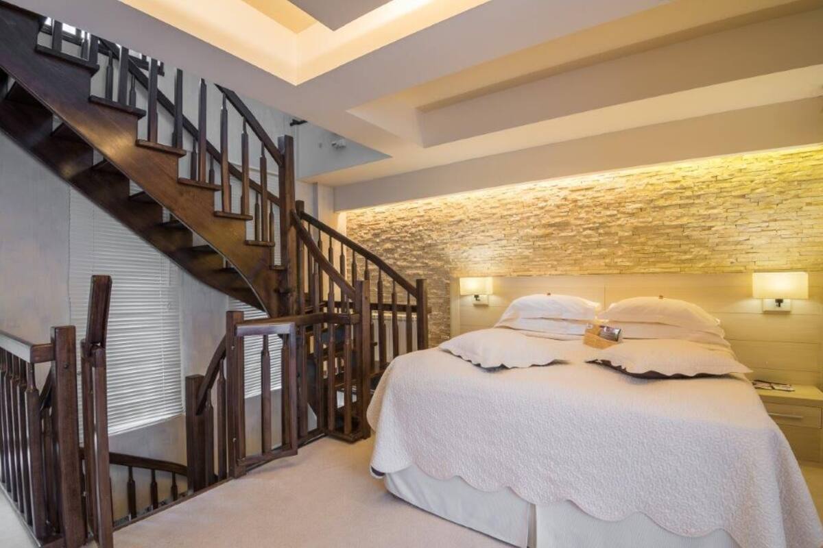 Ein Schlafzimmer mit einer Holztreppe, einer Wand aus Naturstein, einem Bett mit weißer Bettwäsche und Nachttischlampen.