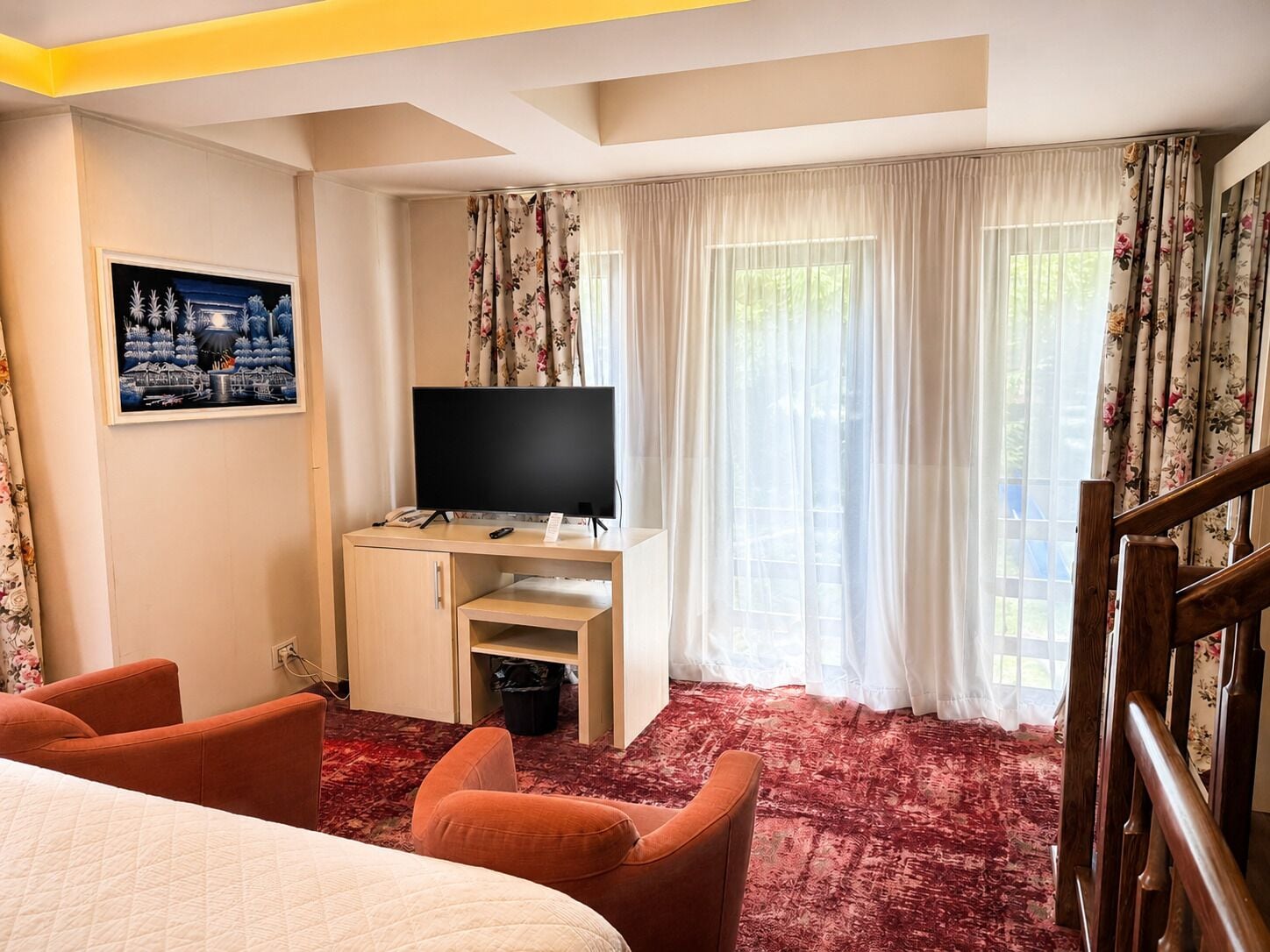A hotel room with a bed, a desk with a TV, a chair, and a staircase.
