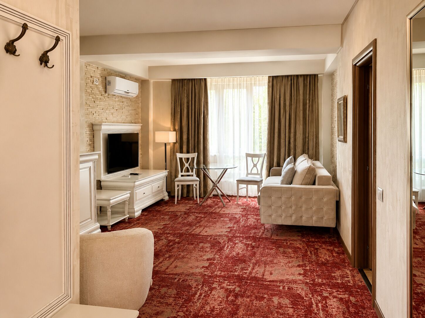 Habitación de hotel con televisor, sofá, mesa de comedor con sillas, chimenea y alfombra roja.