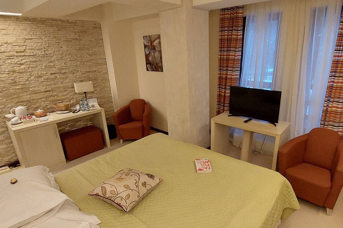 Ein Hotelzimmer mit Bett, Schreibtisch mit Fernseher, Stuhl, Lampe und einem Fenster mit Vorhängen.