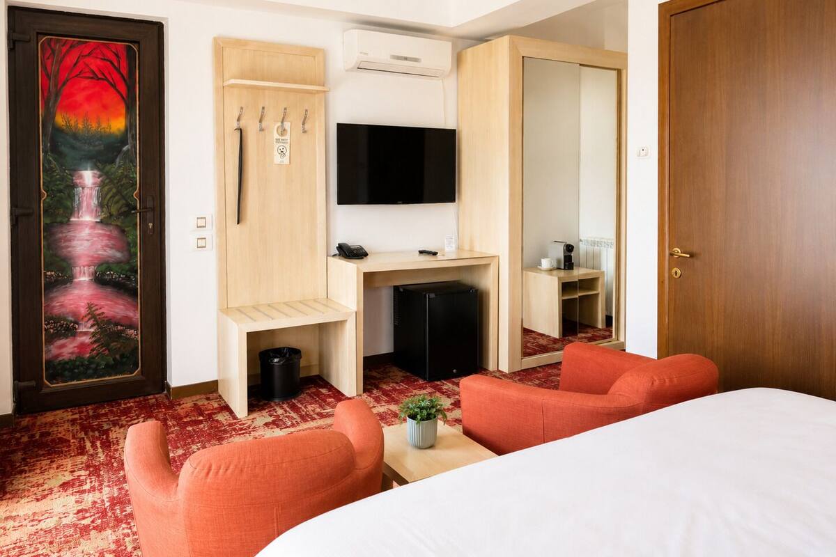 Ein Hotelzimmer mit einem Bett, einem Schreibtisch mit Computer, einem Fernseher, einem Kleiderschrank und einem roten Teppich.