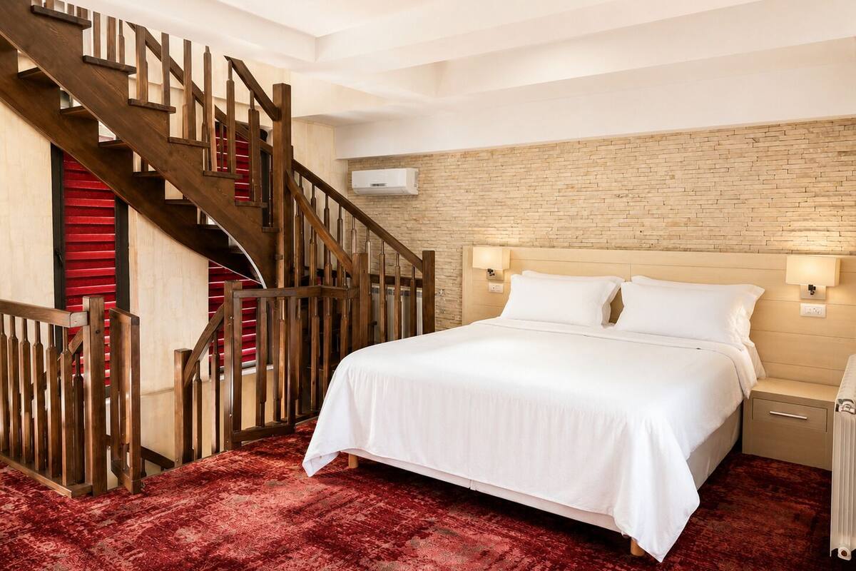 Ein Hotelzimmer mit einem großen Bett, einer Holztreppe, einer Backsteinwand und einem roten Teppich.