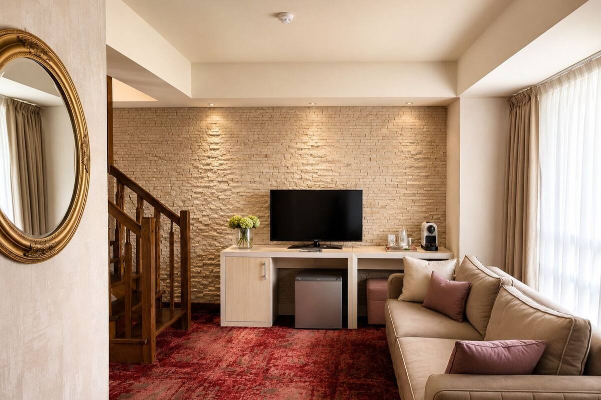 Ein Hotelzimmer mit Backsteinwand, Fernseher, Schreibtisch, Sofa, Spiegel und einer Treppe.