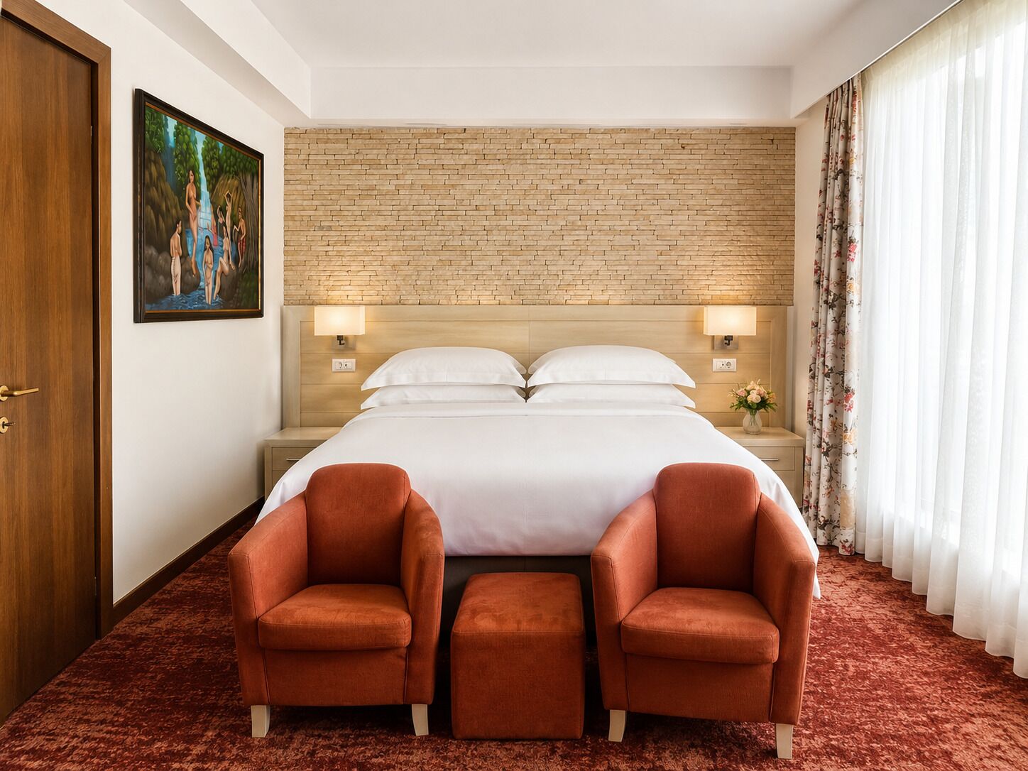Habitación de hotel con pared de ladrillo, cama con ropa blanca, dos sillones rojos y un cuadro en la pared.