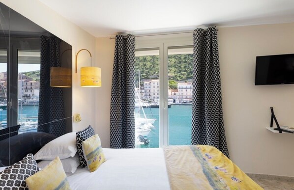 Una camera d'albergo con un letto, una televisione, una lampada e vista sul porto turistico.
