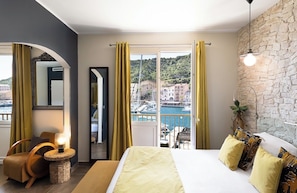 A bedroom with a bed, a chair, a lamp, a mirror, and a view of a marina. - Hotel Solemare (Bonifacio)