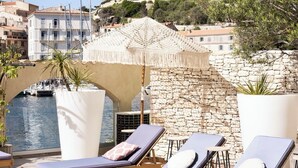 A rooftop lounge with sun loungers, a stone wall, and a view of a historic castle. - Hotel Solemare (Bonifacio)
