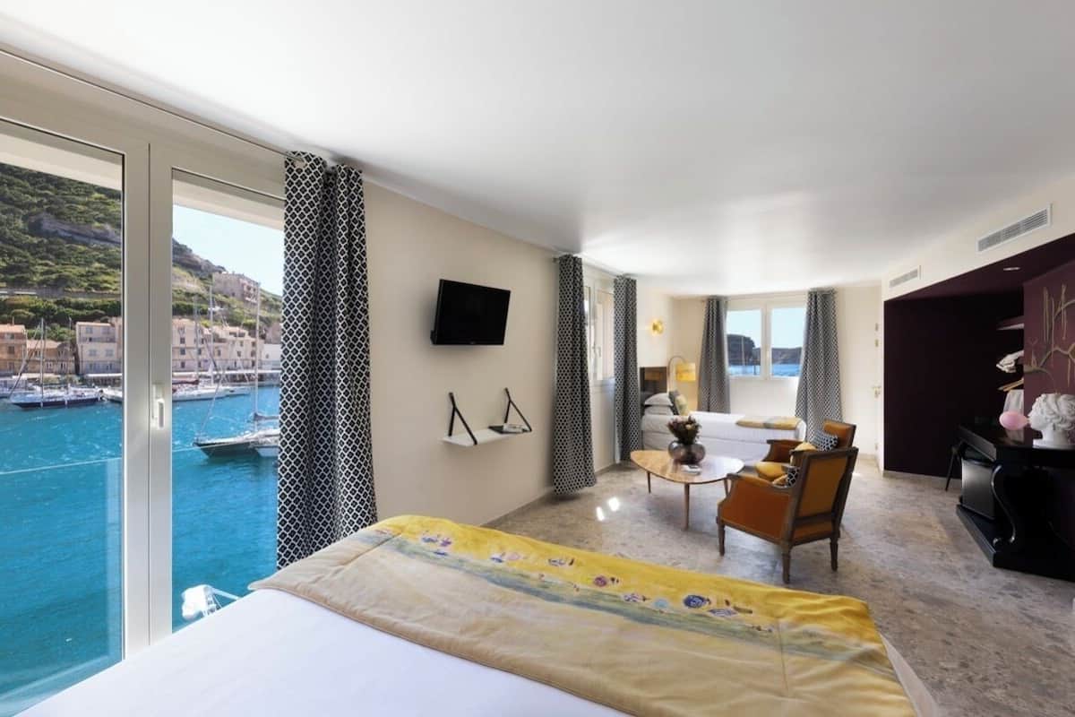 Habitación de hotel con cama, una mesita, una silla, televisión y vista al mar.