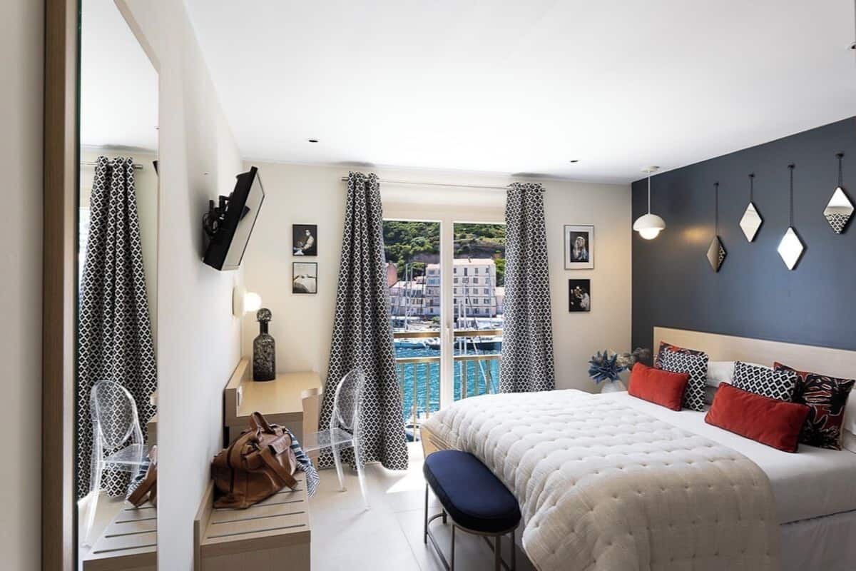 Un dormitorio con cama, un banco, una silla, un televisor y vista al agua.
