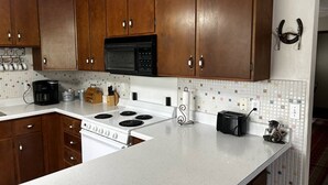 A kitchen with wooden cabinets, a white countertop, a stove, a microwave, and a coffee maker.
