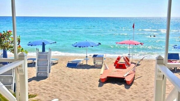 A beach with umbrellas, lounge chairs, and a lifeguard stand.