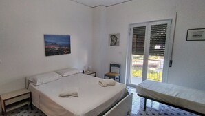 A bedroom with a bed, a chair, a nightstand, a window with blinds, and a balcony.