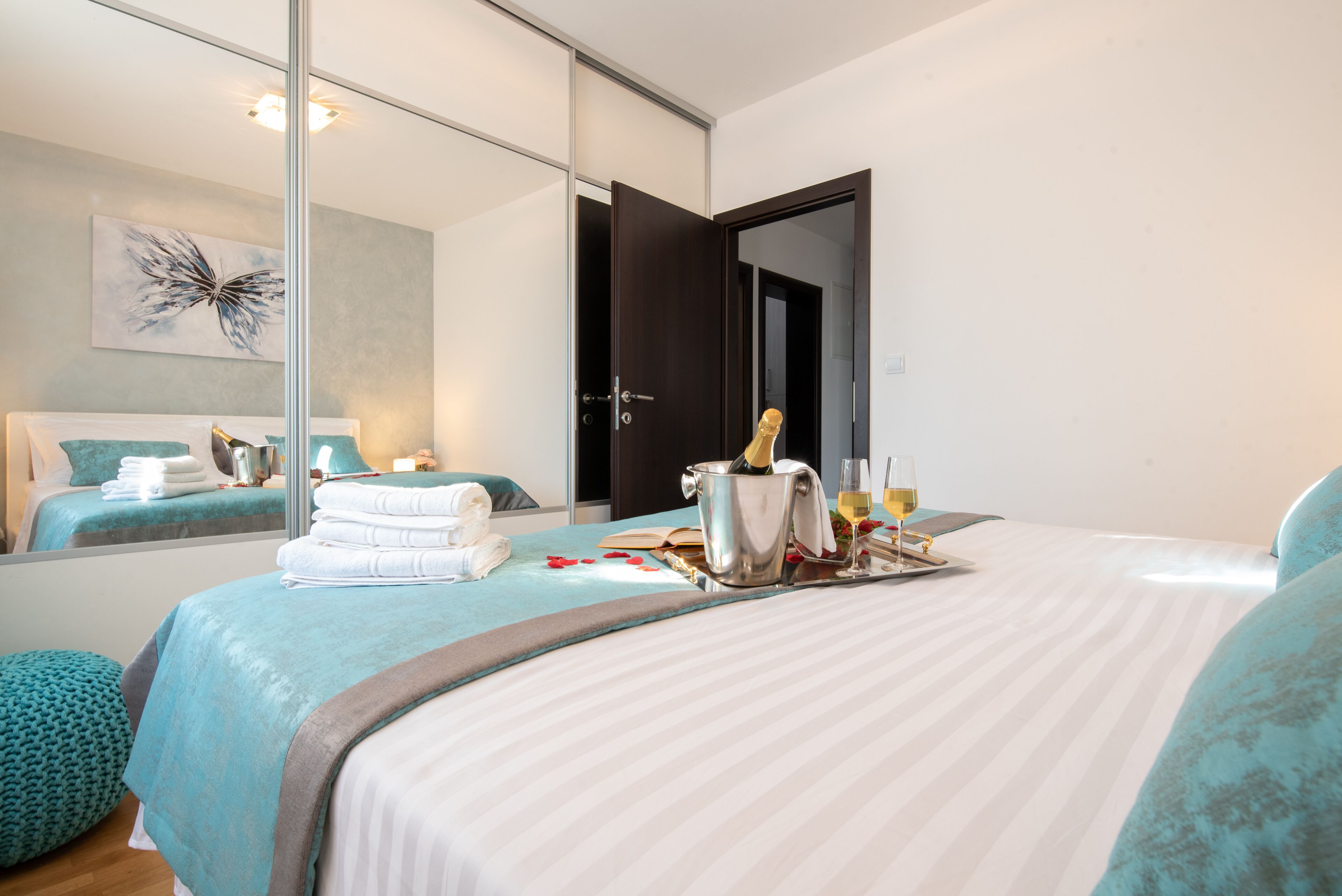A hotel room with a bed, a large mirror, a minibar, and a door leading to another room.