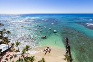 Relax on the beach with umbrellas and lounge chairs, surrounded by boats and a natural breakwater.