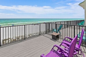 Une terrasse en bois avec une rambarde, des chaises violettes et une vue sur la plage.