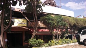 A building with a sign for 'SUNSET TUSKER' and a reception area. There is a tree in the foreground and a parked vehicle to the right. - Sunset View Complex (Mombasa)
