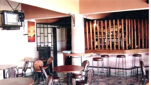 A bar area with stools and tables, a television mounted on the wall, and a patterned floor. - Sunset View Complex (Mombasa)