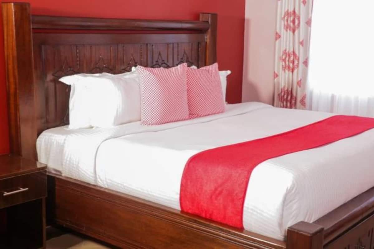 Una cama bien hecha con cabecera de madera, ropa blanca y una manta roja.