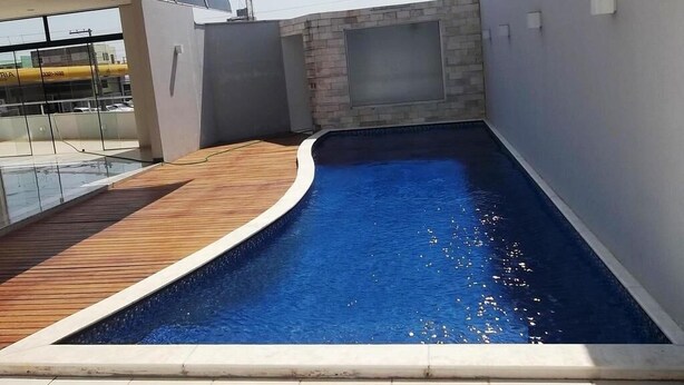A rooftop swimming pool with a wooden deck and a stone wall. - Hotel Portinari (Vilhena)