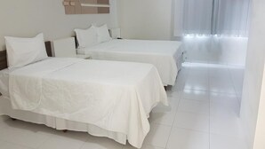 A hotel room with two beds, a bedside table, a wall-mounted shelf, and a large window with sheer curtains. - Hotel Portinari (Vilhena)