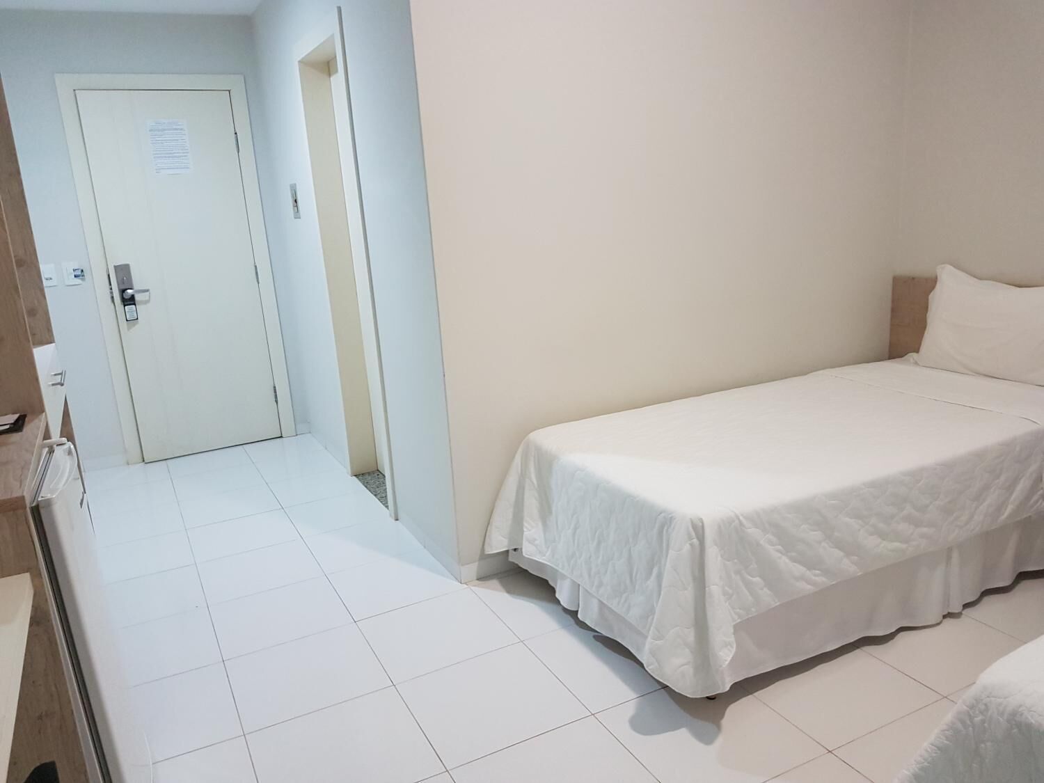 Una habitación pequeña y limpia con una cama individual, una puerta y piso de baldosas.