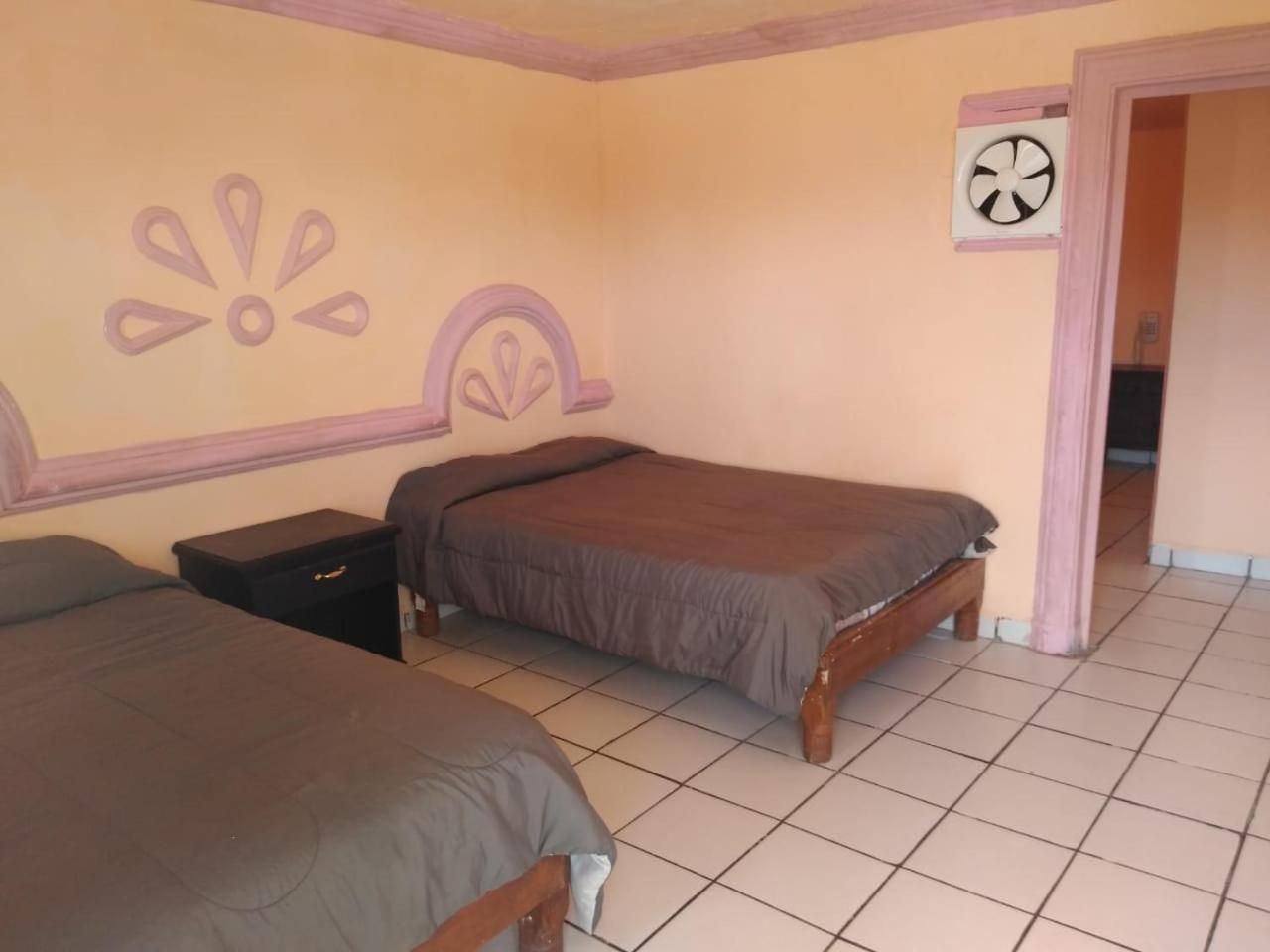 A bedroom with two beds, a nightstand, and a door leading to another room.