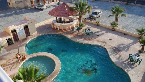 A swimming pool with a sunshade, palm trees, and outdoor seating. - Hotel Plaza Peñasco (Puerto Peñasco)