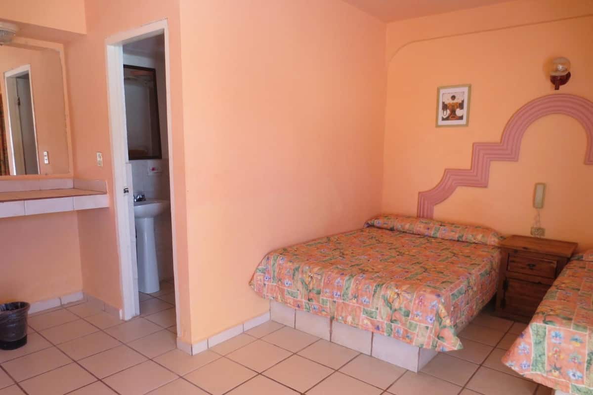 A bedroom with a bed, a nightstand, a dresser, a mirror, and a door leading to a bathroom.