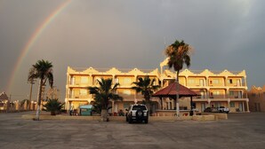 A hotel with a parking lot, palm trees, and a rainbow in the sky. - Hotel Plaza Peñasco (Puerto Peñasco)