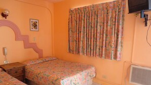 A bedroom with two beds, a wall-mounted TV, and a window with floral curtains. - Hotel Plaza Peñasco (Puerto Peñasco)