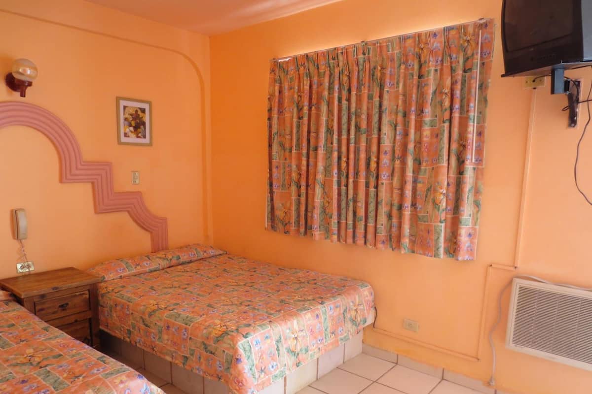 A bedroom with two beds, a wall-mounted TV, and a window with floral curtains.