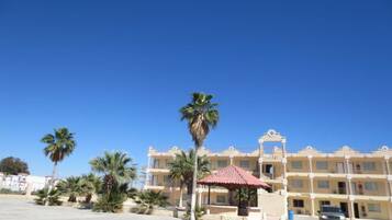 A multi-story hotel with a central courtyard, palm trees, and a red-roofed gazebo.