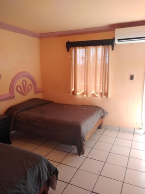 A room with a bed, a nightstand, a window with curtains, and an air conditioning unit.