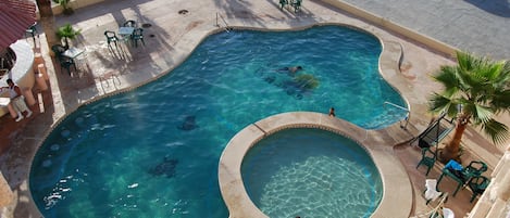 A swimming pool with a circular hot tub, surrounded by palm trees and outdoor seating.