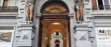 A grand entrance with two statues on either side, an ornate archway, and a sign for a business office.
