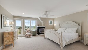 A bedroom with a large bed, a ceiling fan, a fireplace, and a view of the outdoors. - Gorgeous home sleeping 12 with ocean views (West Harwich)