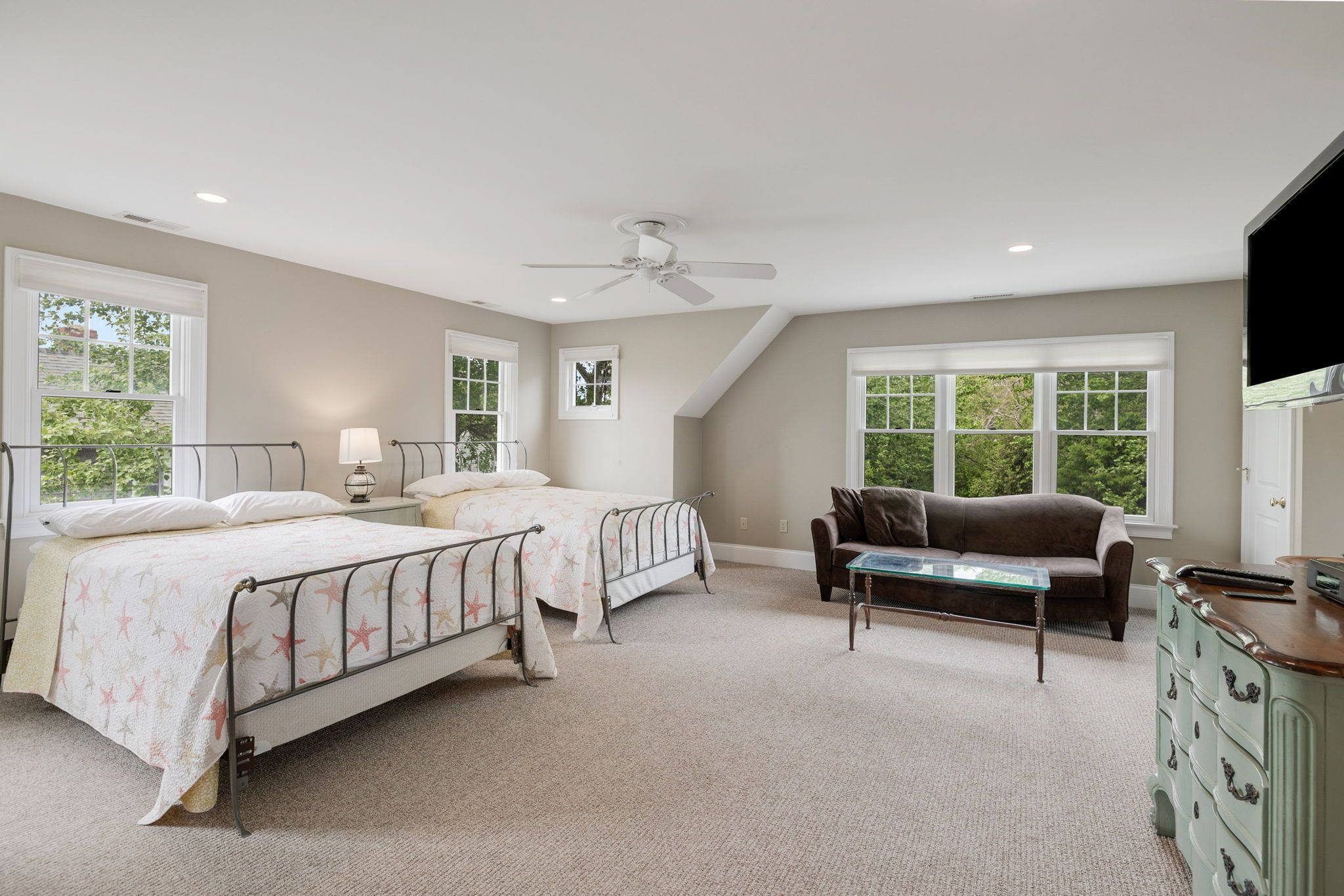 Une chambre avec deux lits, un ventilateur de plafond, une commode, un canapé et de grandes fenêtres.